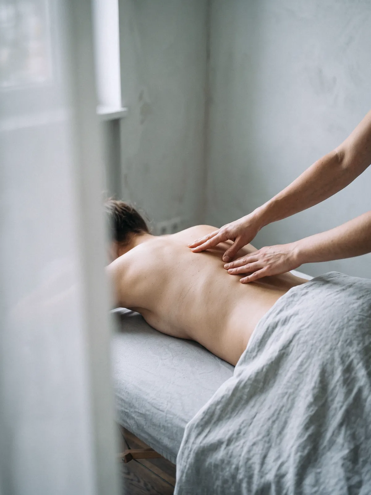Die Hände einer Osteopathin ertasten die Wirbel entlang der Wirbelsäule einer liegenden Patientin.